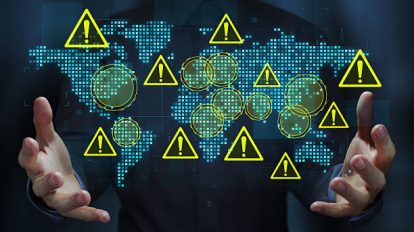 Business person holding a world map and warning triangle icons.