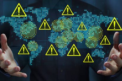 Business person holding a world map and warning triangle icons.