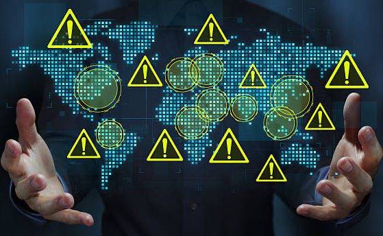 Business person holding a world map and warning triangle icons.